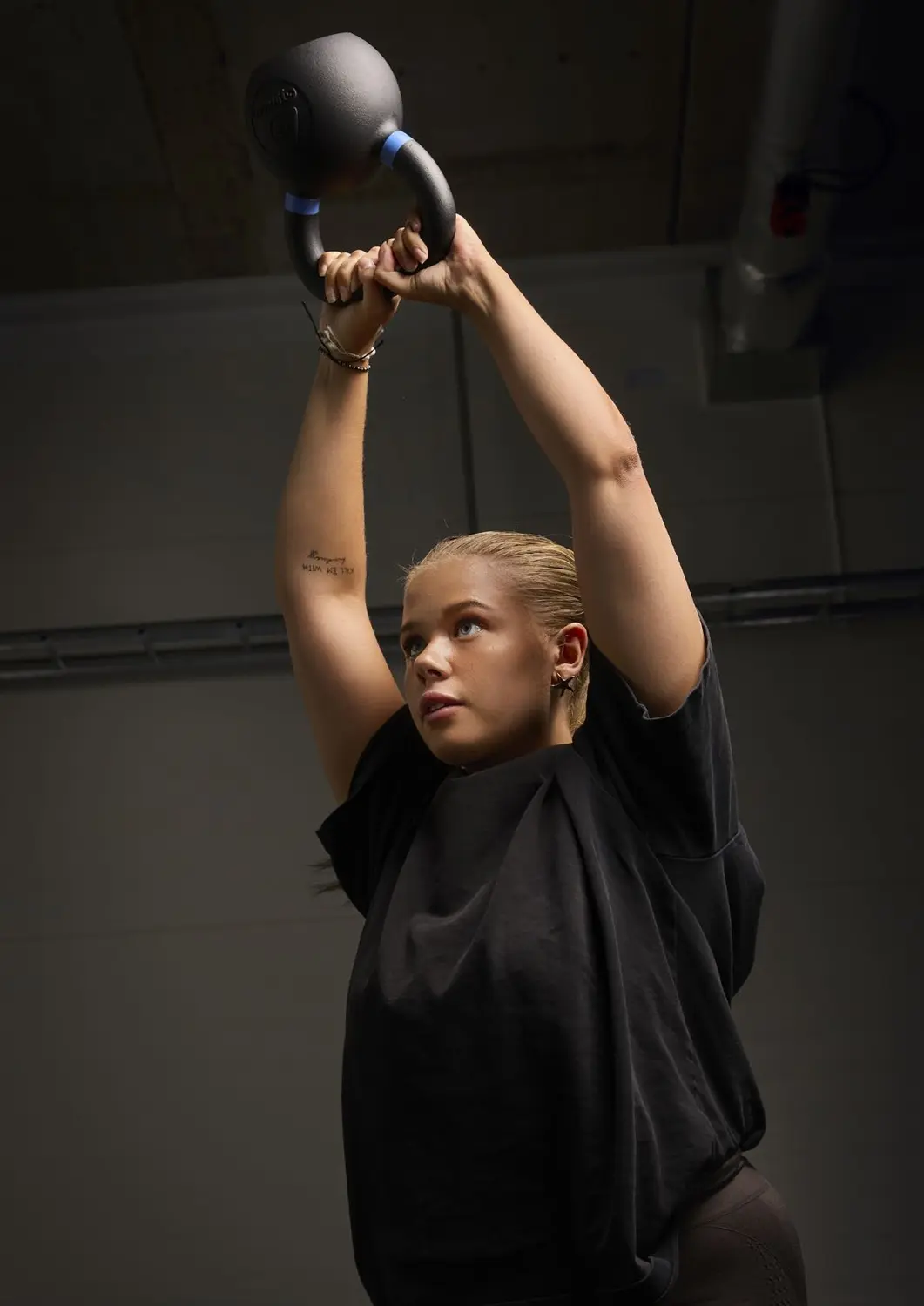 מתאמנת מניפה קטלבל של Gymleco מעל הראש
